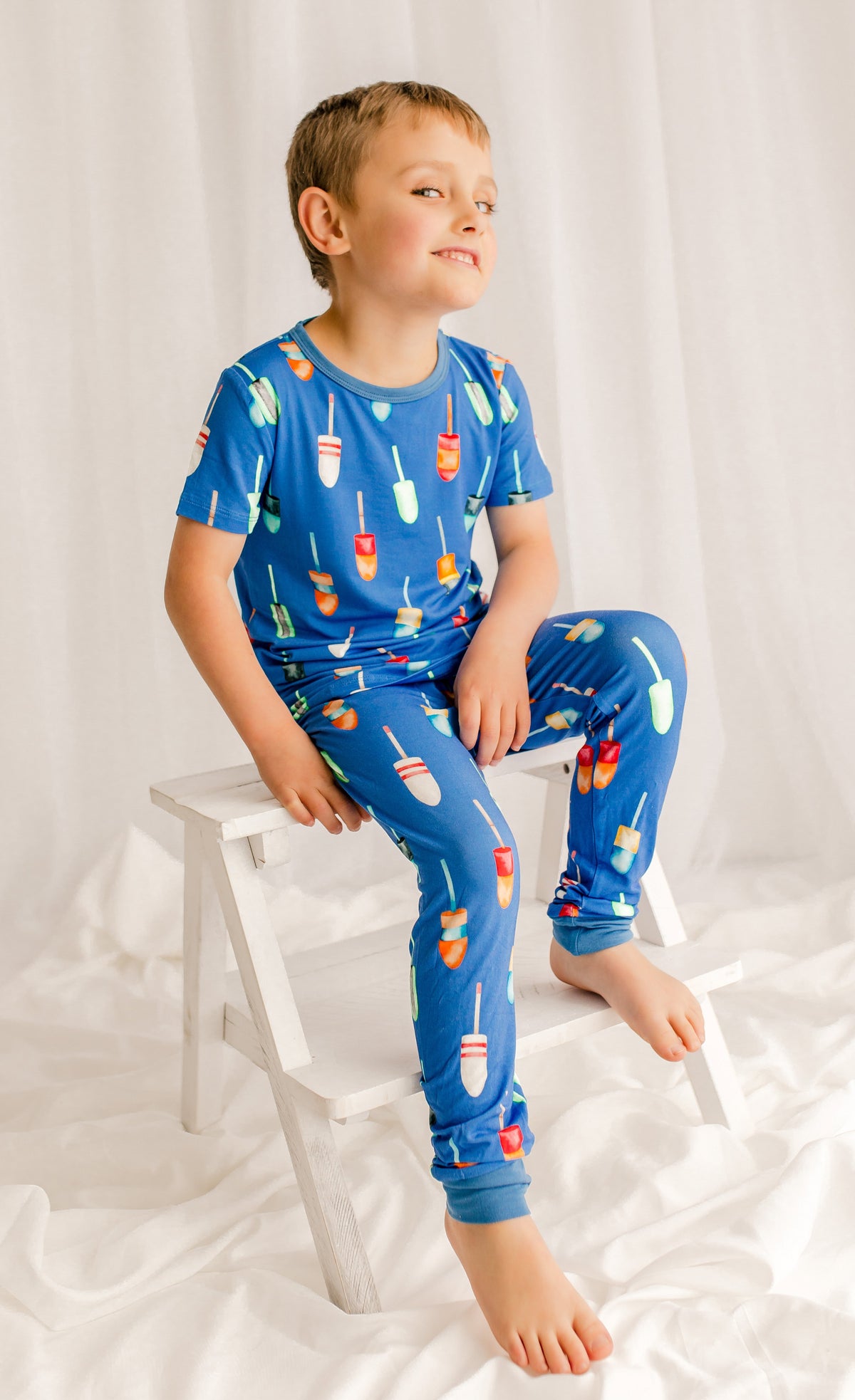 Child wearing short sleeved top and long pants with a blue background with all kinds of colorful buoys 