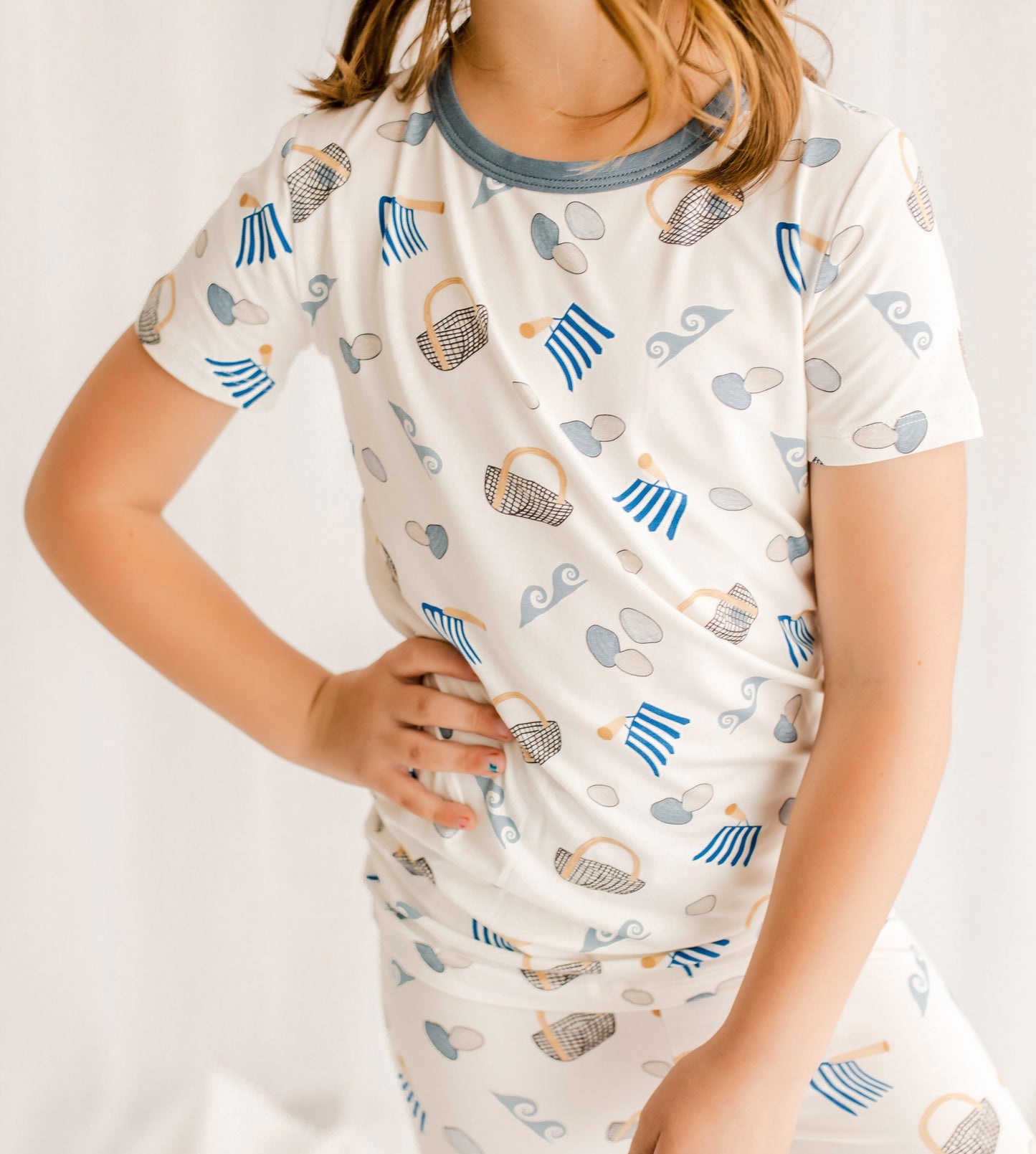 Child wearing a short sleeve pajama set with clams, diggers, baskets, and waves with gray cuffs on a white background 