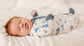 Newborn baby wearing a onesie with blue, gray, and tan prints of clams, baskets, waves, and clams on a white background. 