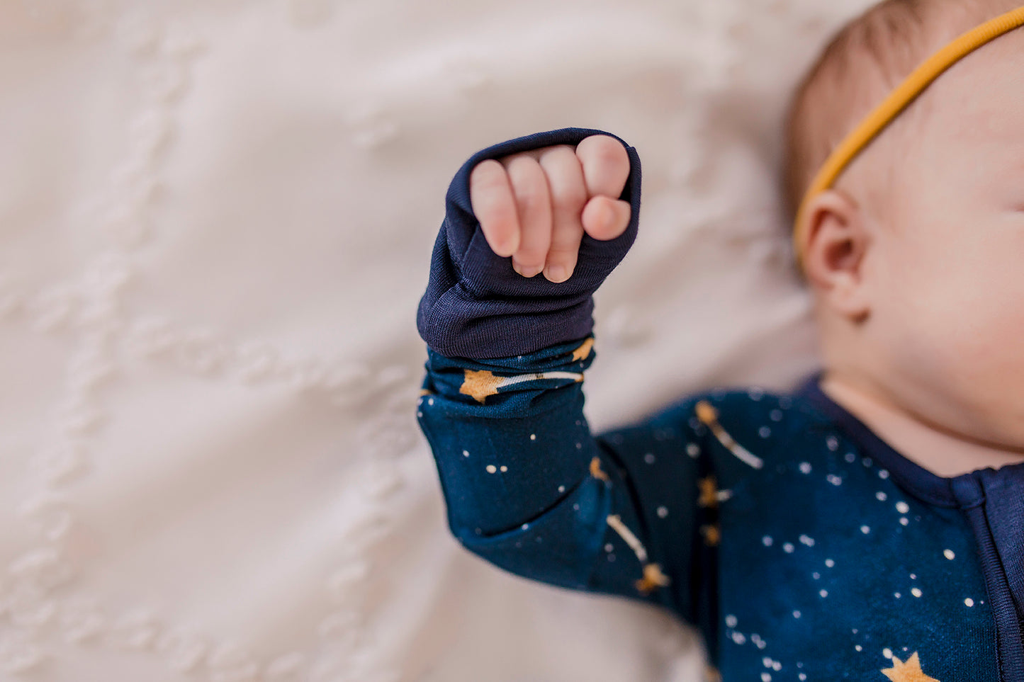 Baby wearing constellation themed dark blue long sleeve zippy that shows the little dipper, big dipper, the galaxy, and stars on a Maine September night with blue cuffs 
