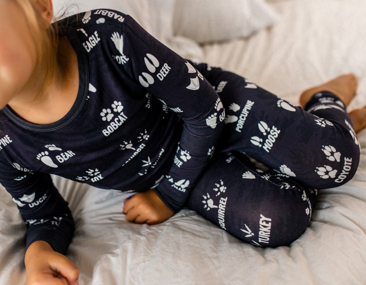 Child wearing charcoal two piece pajamas set with white wildlife tracks on a bed 