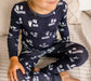 Child wearing gray two piece organic bamboo pajamas with white animal prints sitting cross legged on a couch