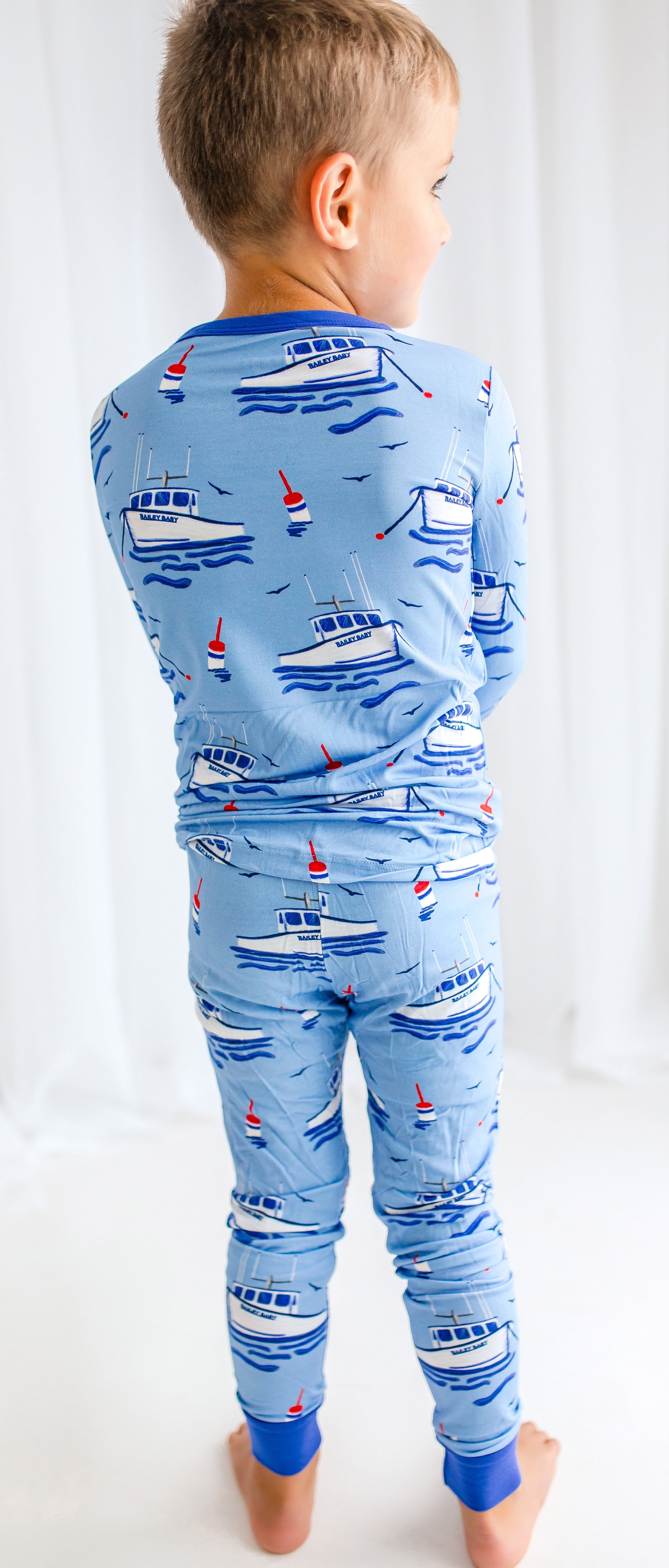 Child wearing blue pajamas with Maine fishing lobster boats, floating buoys, waves, and flying seagulls on the atlantic ocean 