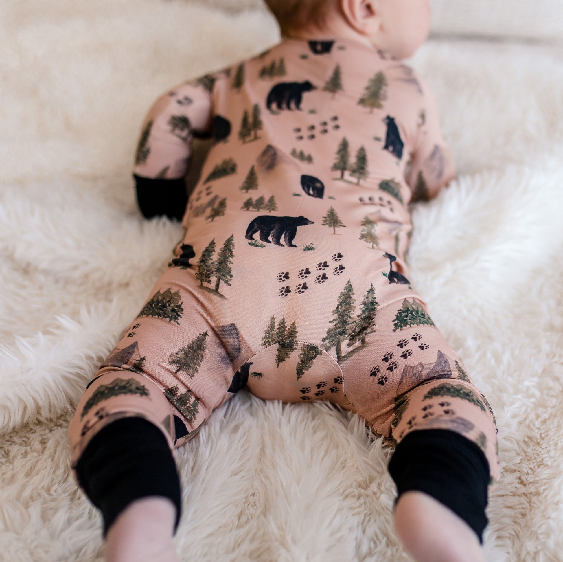 Baby wearing a onesie with black bears, and green trees from the Maine forest, mountains, and bear tracks. 