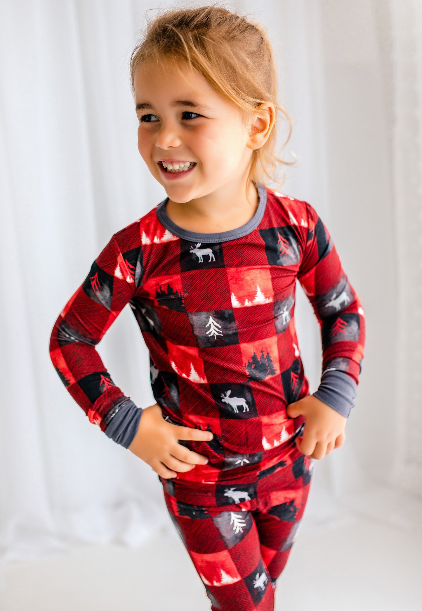 Child wearing red plaid two piece pajama set with trees from the Maine forest and white moose 