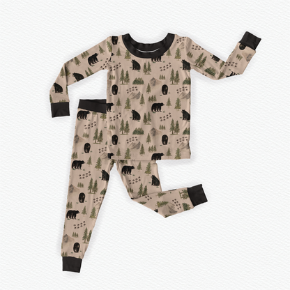 Children's pajama set with bears, vast gray mountains, green trees, and animal tracks on a beige background with black accents
