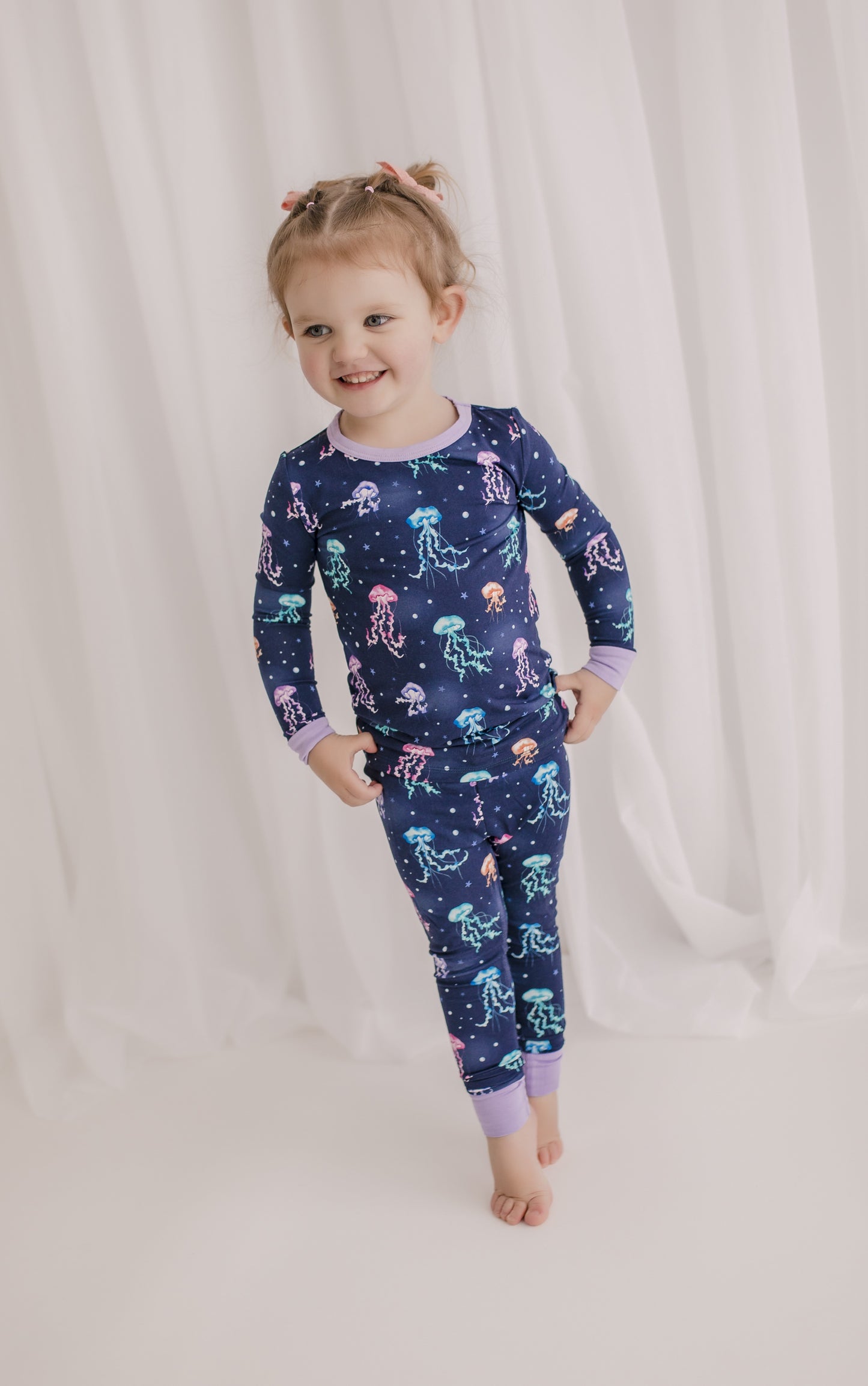 Child wearing two piece pajama set with a jellyfish theme with colors of purple, pink, orange, and teal. 