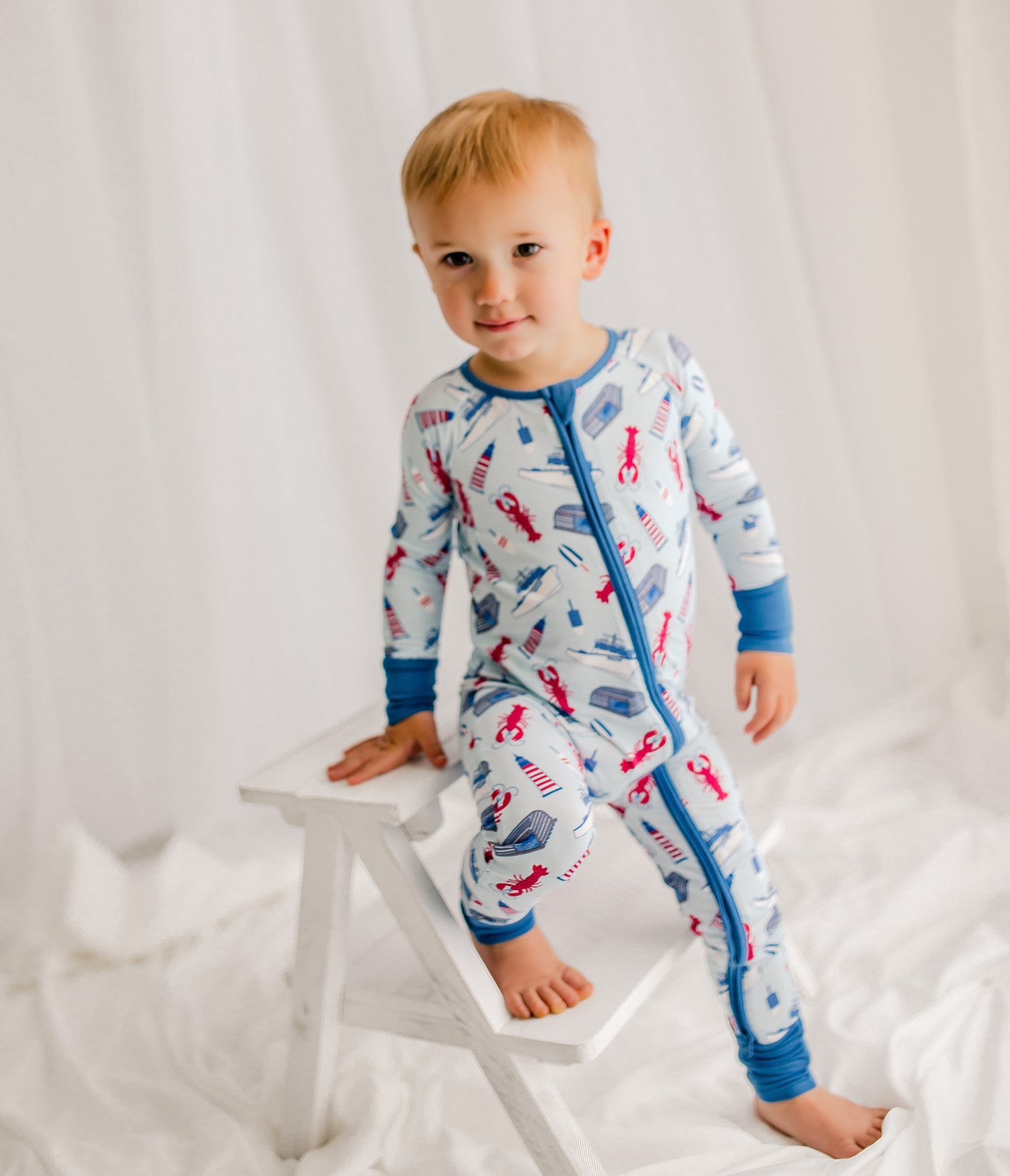 Child wearing a maine themed lobster fishing one piece with a light blue background and a darker blue on the cuffs 