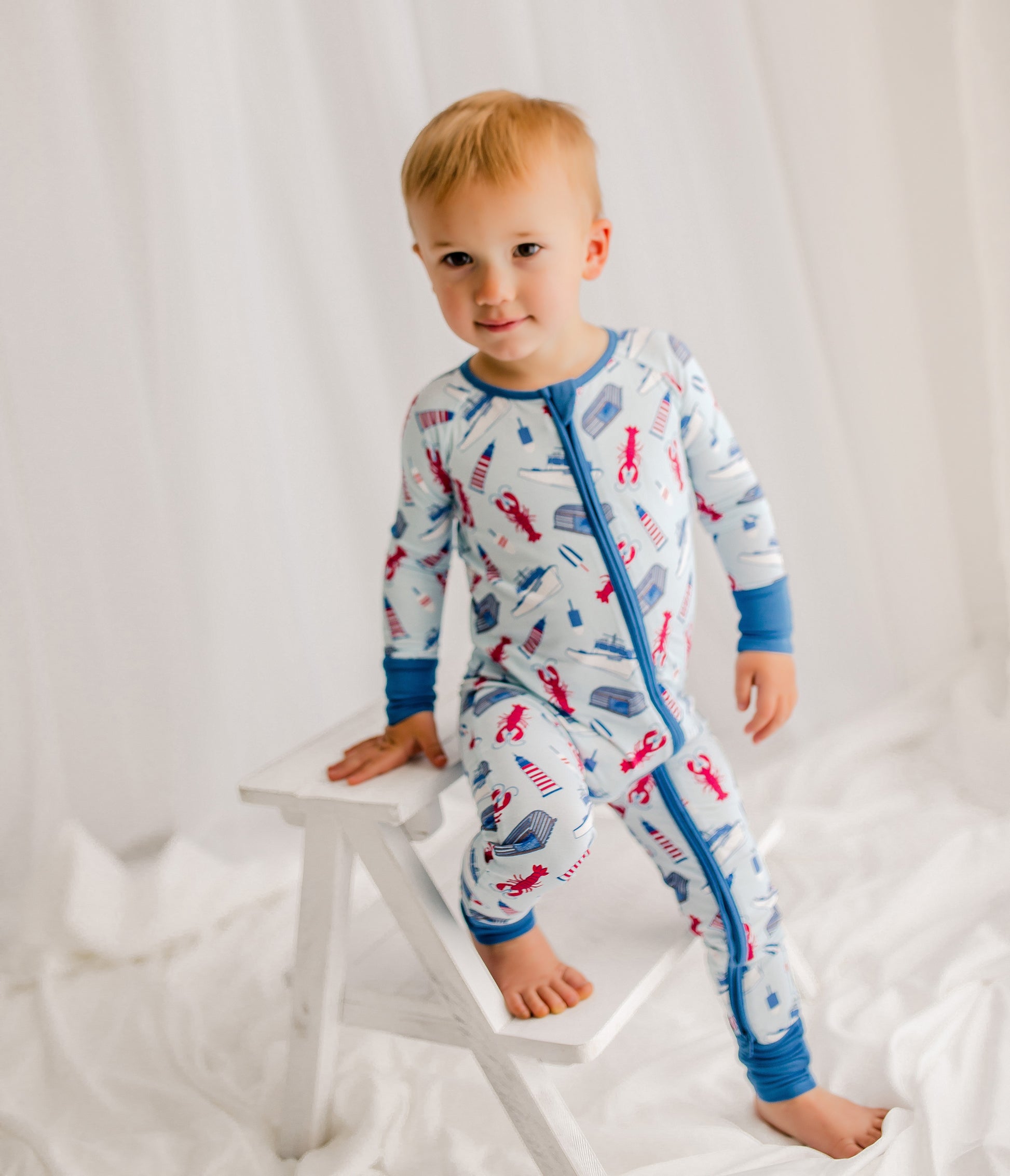 Child wearing a maine themed lobster fishing one piece with a light blue background and a darker blue on the cuffs 