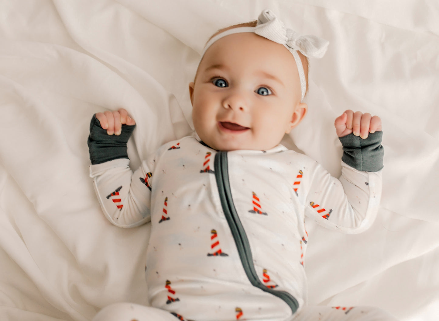 Baby wearing a one piece zippy romper with black cuffs, a white background, and red and white lighthouses all over 