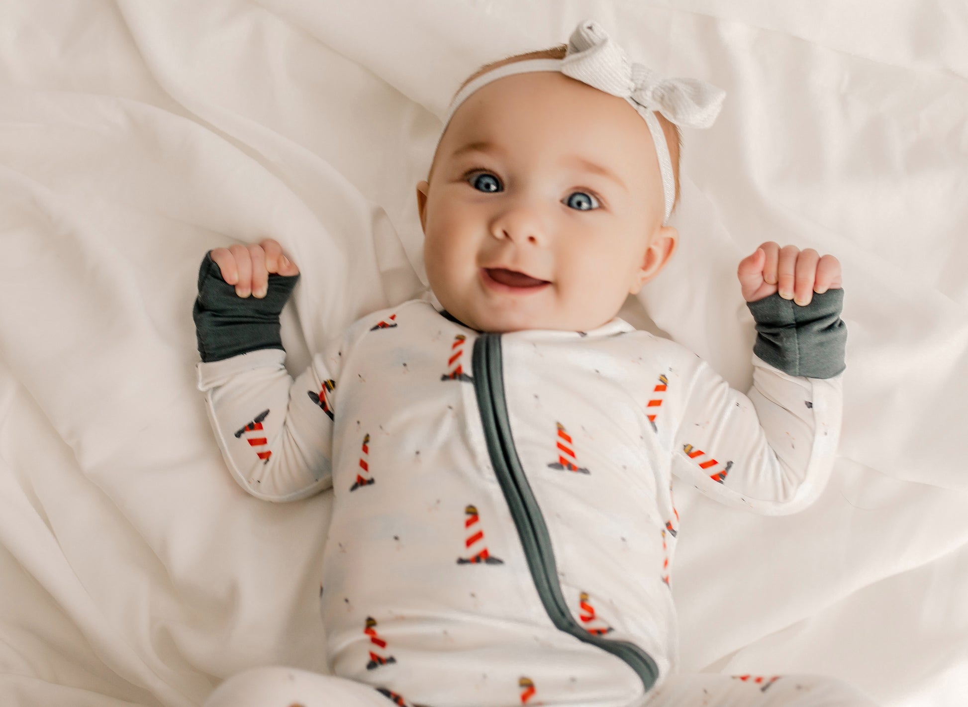 Baby wearing a one piece zippy romper with black cuffs, a white background, and red and white lighthouses all over 