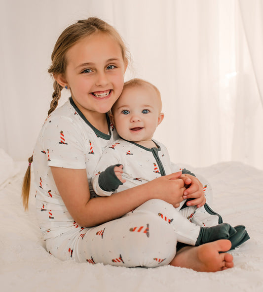 Two children in matching pajamas of Maine Lighthouses that are red and white with black accents 