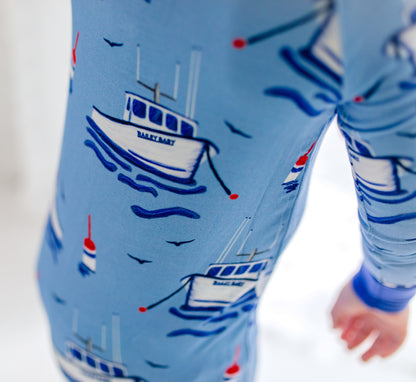 Children's light blue onesie with darker blue accents with fishing boats, floating red blue and white buoys, flying seagulls, and waves under the boats. 