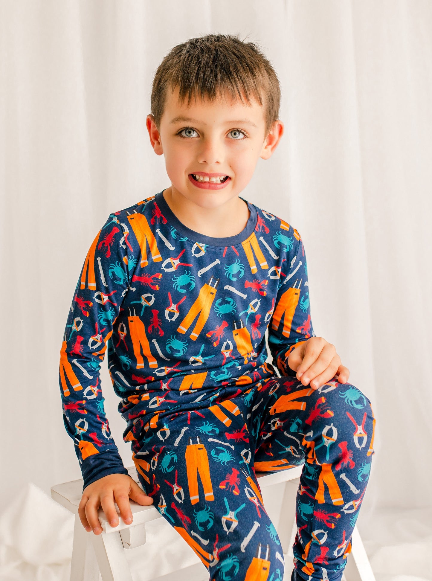 Child wearing a colorful pajama set with lobsters, crabs, and all the essentials for working on a lobster boat 