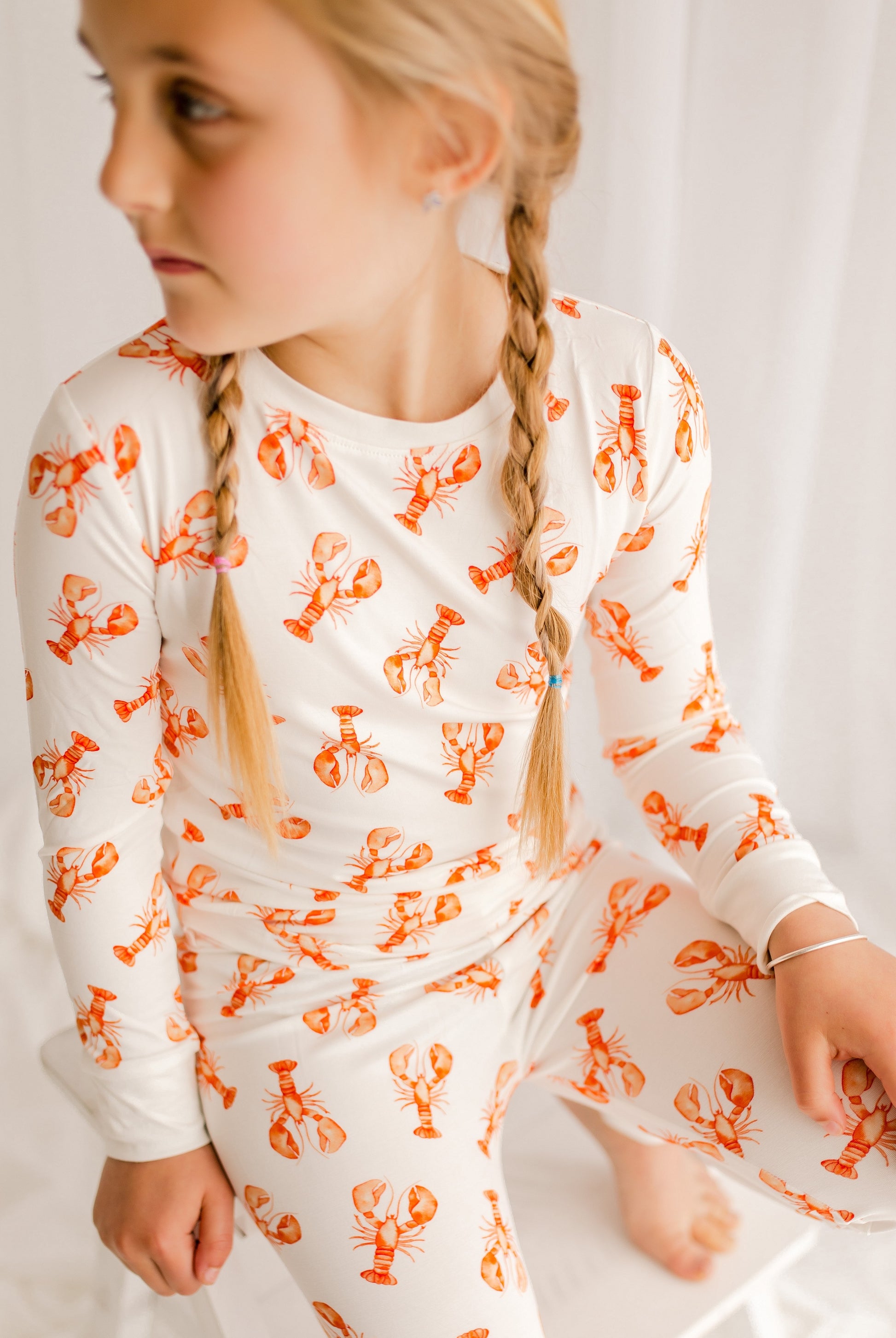 Young girl wearing a white long-sleeve pajama set with orange lobster pattern.