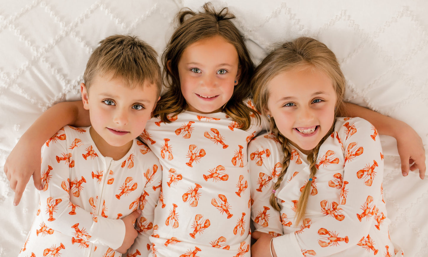 Children wearing a white one piece with orange lobster patterns on a white background