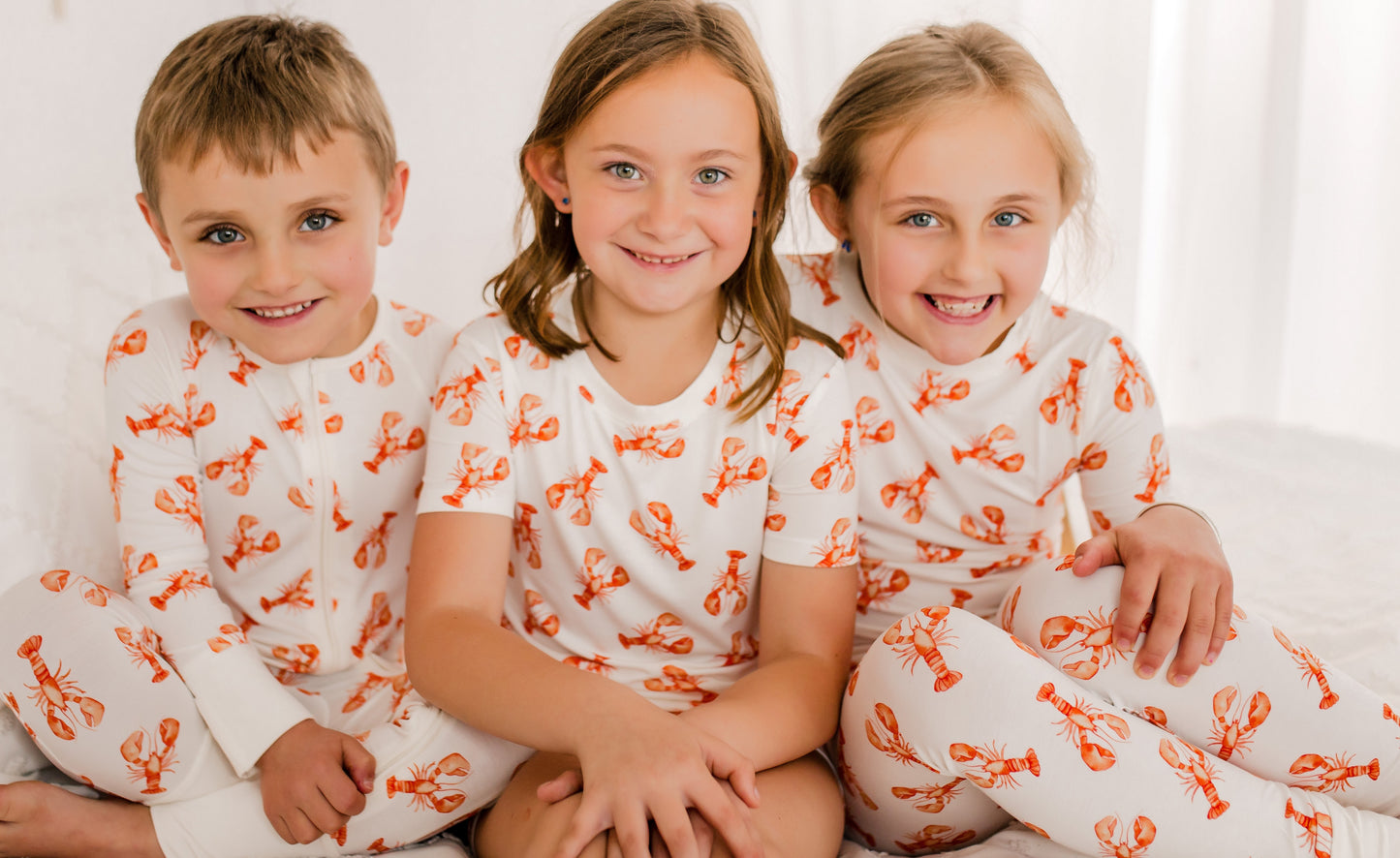 Three children wearing matching pajamas with orange lobsters caught in Maine