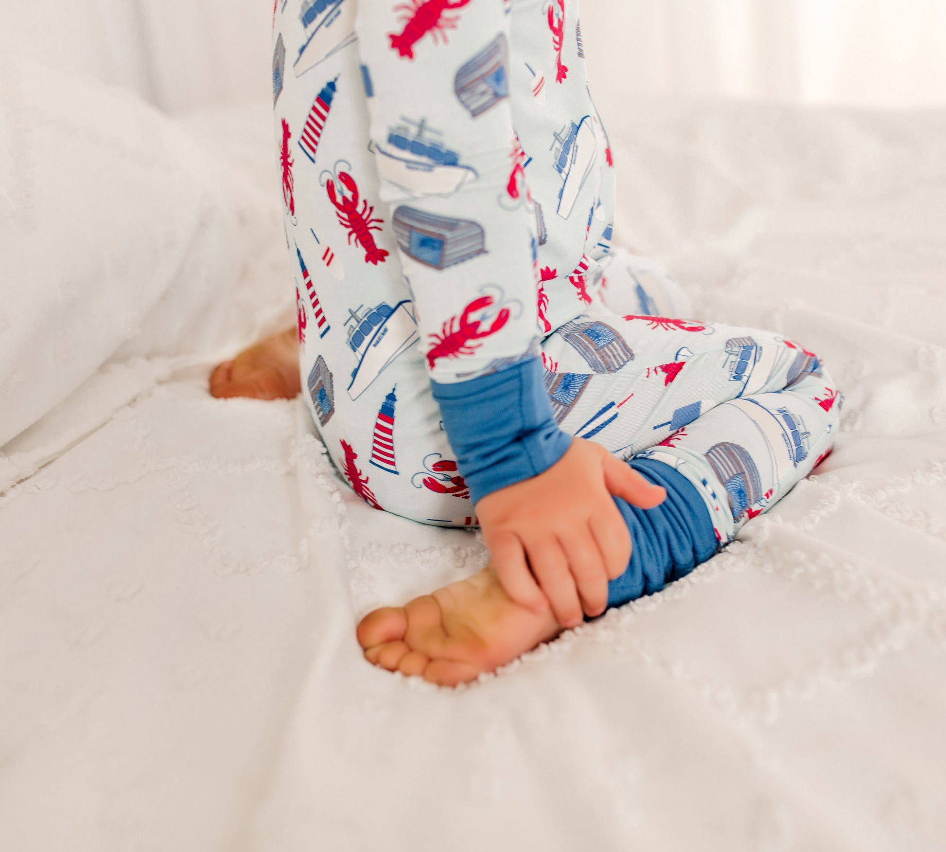 Child wearing a patterned onesie featuring maine lobsters, boats, lighthouses, and buoys 