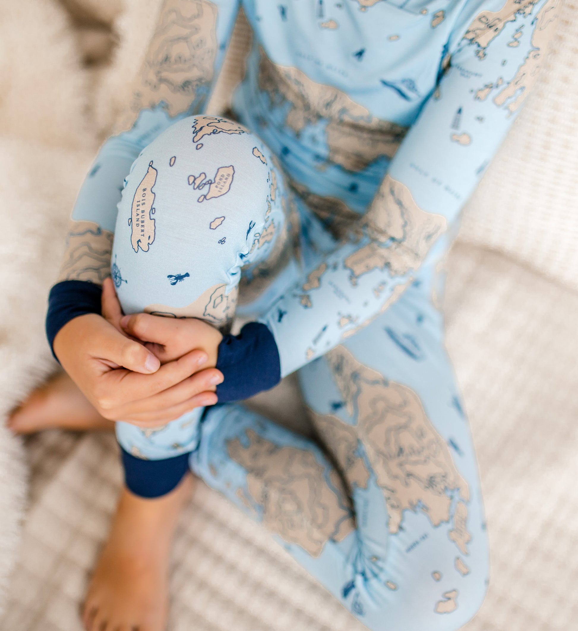 Child wearing a light blue two piece with a cream colored nautical map with blue lobsters, compass, and lobster boats. 