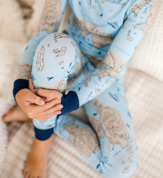 Child wearing a light blue two piece with a cream colored nautical map with blue lobsters, compass, and lobster boats. 