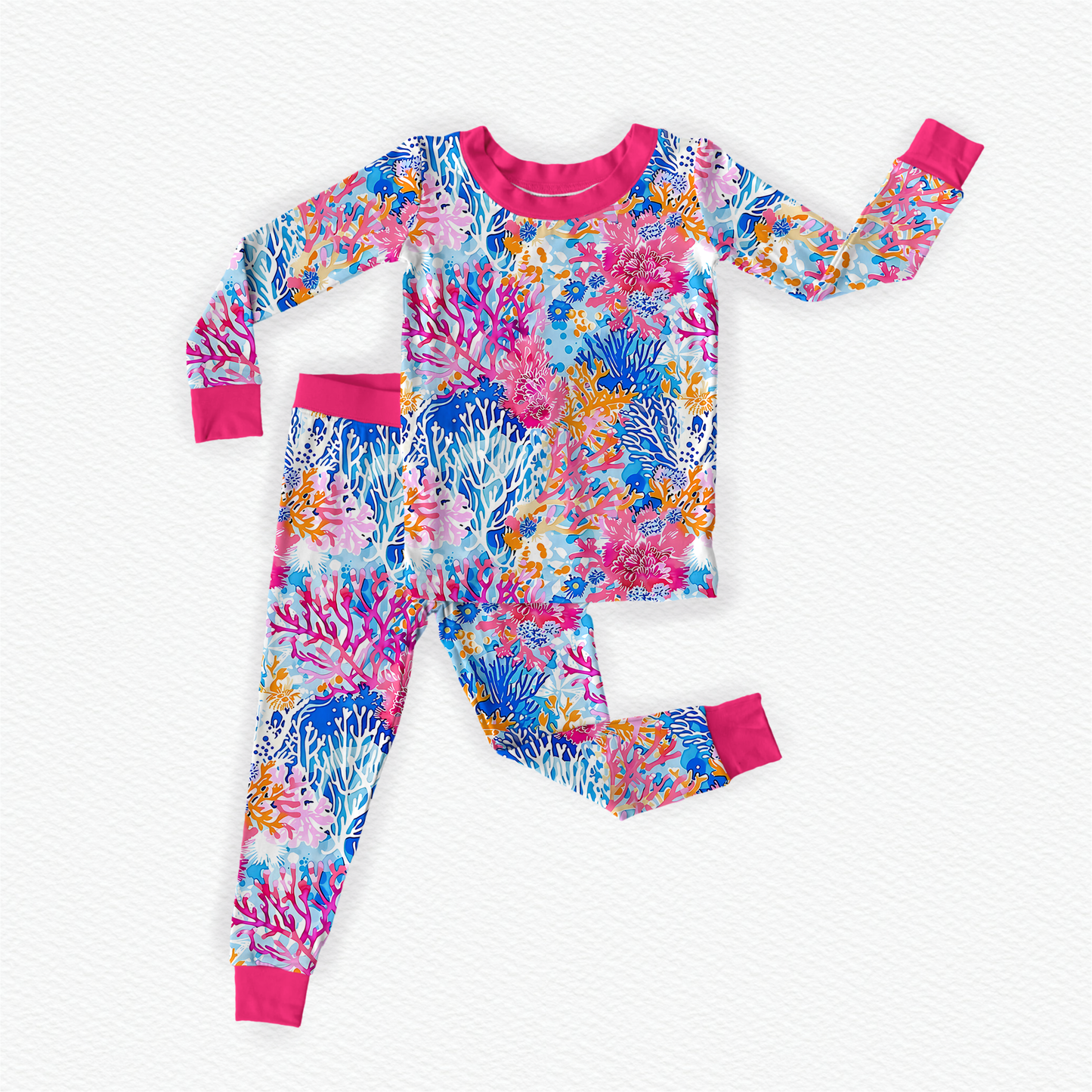 A child wearing a long sleeve top and pants with a vibrant coral reef design in multiple pink shades along with different blues and oranges. 