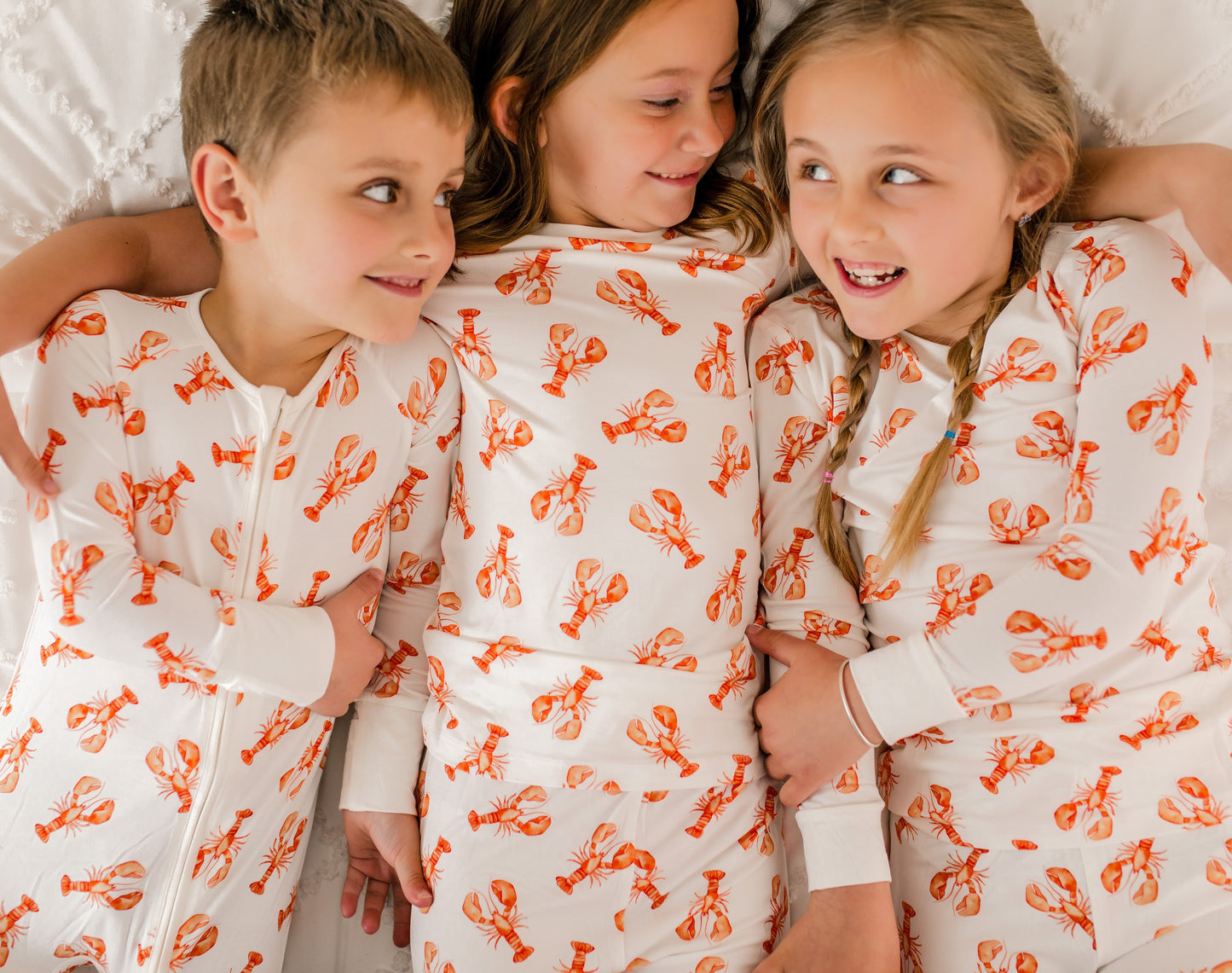 Three children wearing white pajamas with orange lobster patterns