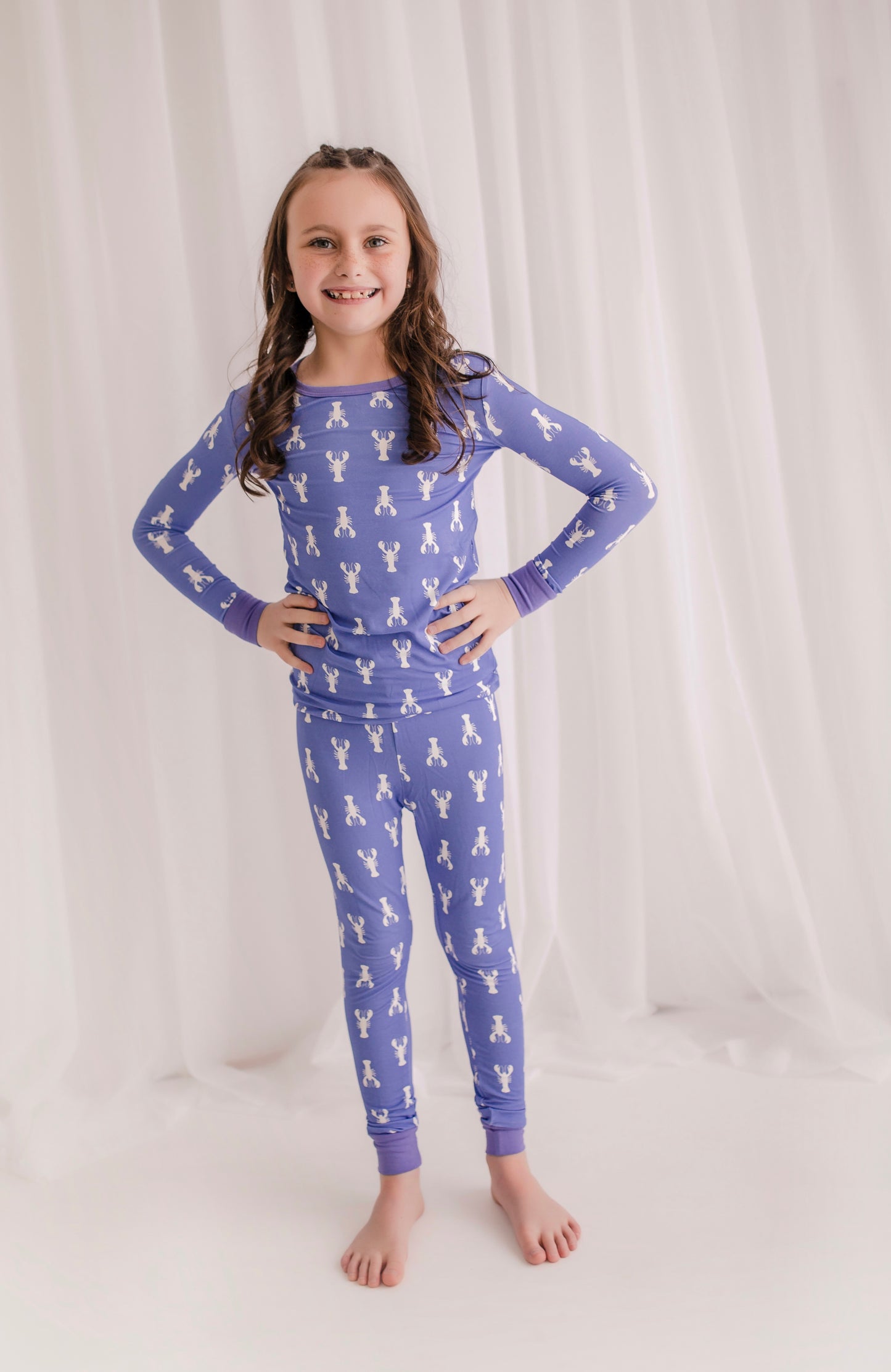 Child wearing purple pajamas with white maine lobsters, with purple cuffs 