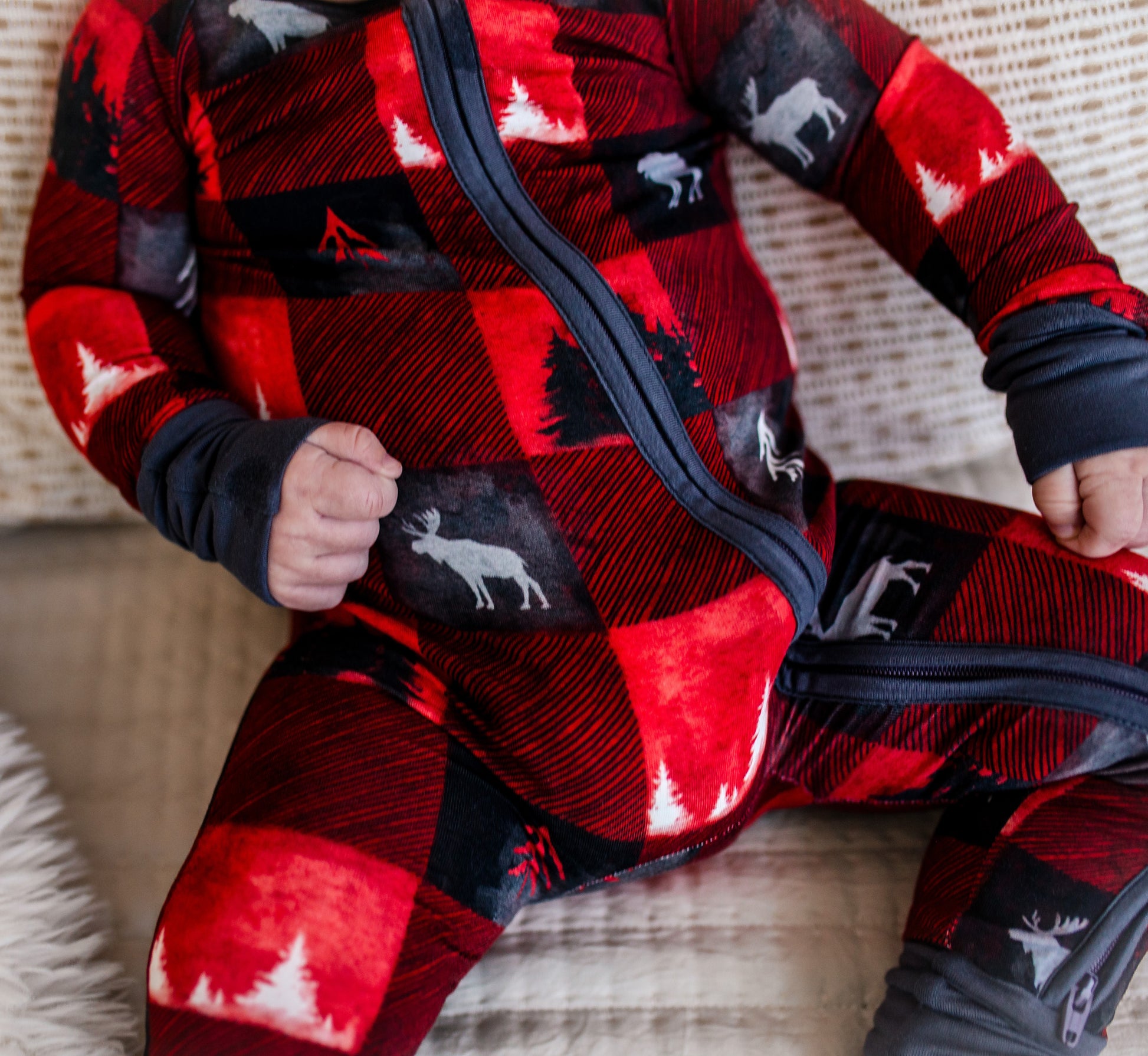Child wearing a red and black checkered zippy romper with one of Maines icons, the moose and different kinds of trees in black and white
