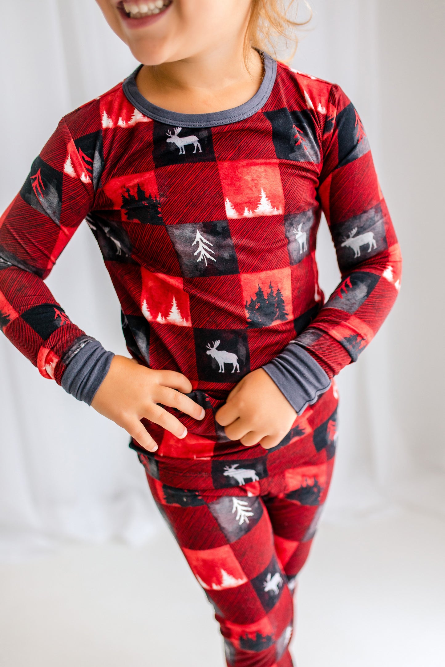 Red plaid themed pajamas with black and red squares with white moose and white and black trees and gray accents 