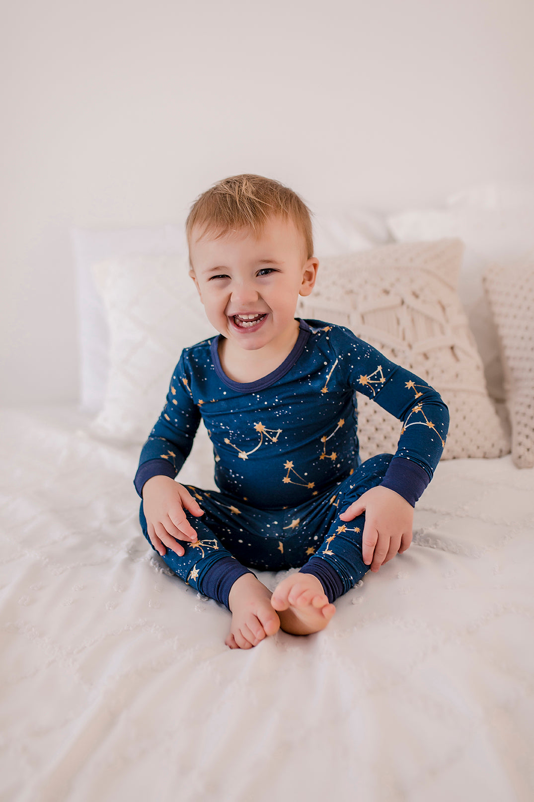 A toddler wearing a two-piece pajama set with a dark blue background and gold constellation prints.