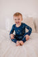 A toddler wearing a two-piece pajama set with a dark blue background and gold constellation prints.