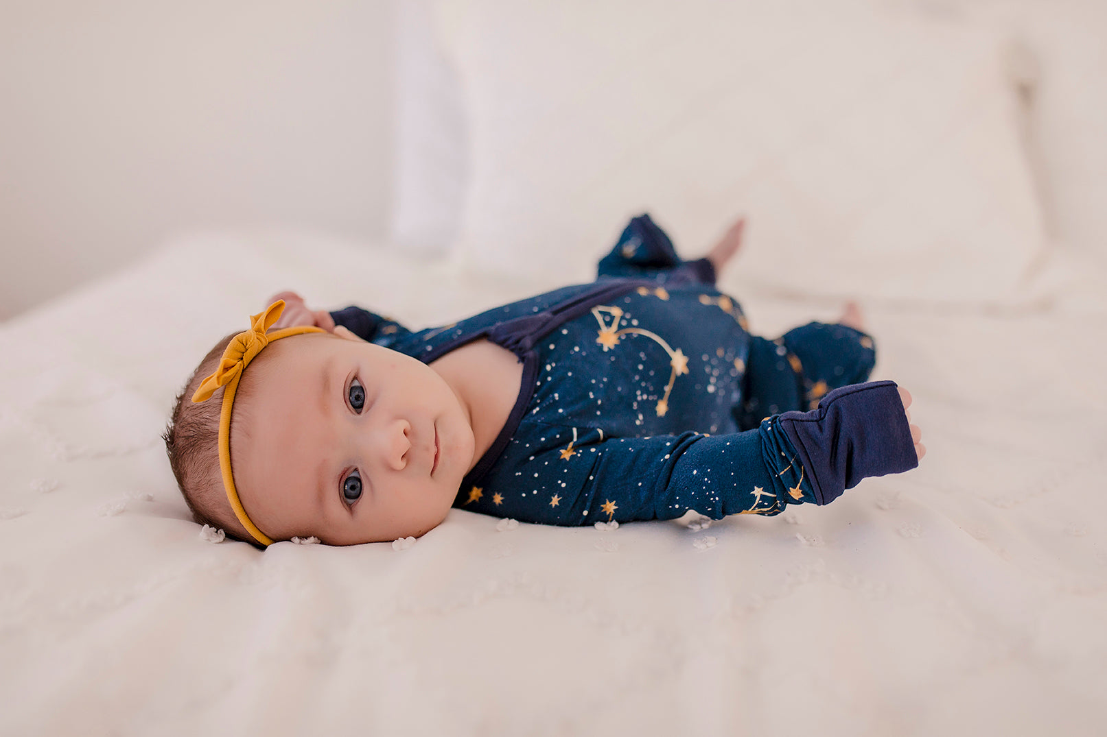 Baby wearing constellation themed dark blue long sleeve zippy that shows the little dipper, big dipper, the galaxy, and stars on a Maine September night with blue cuffs 