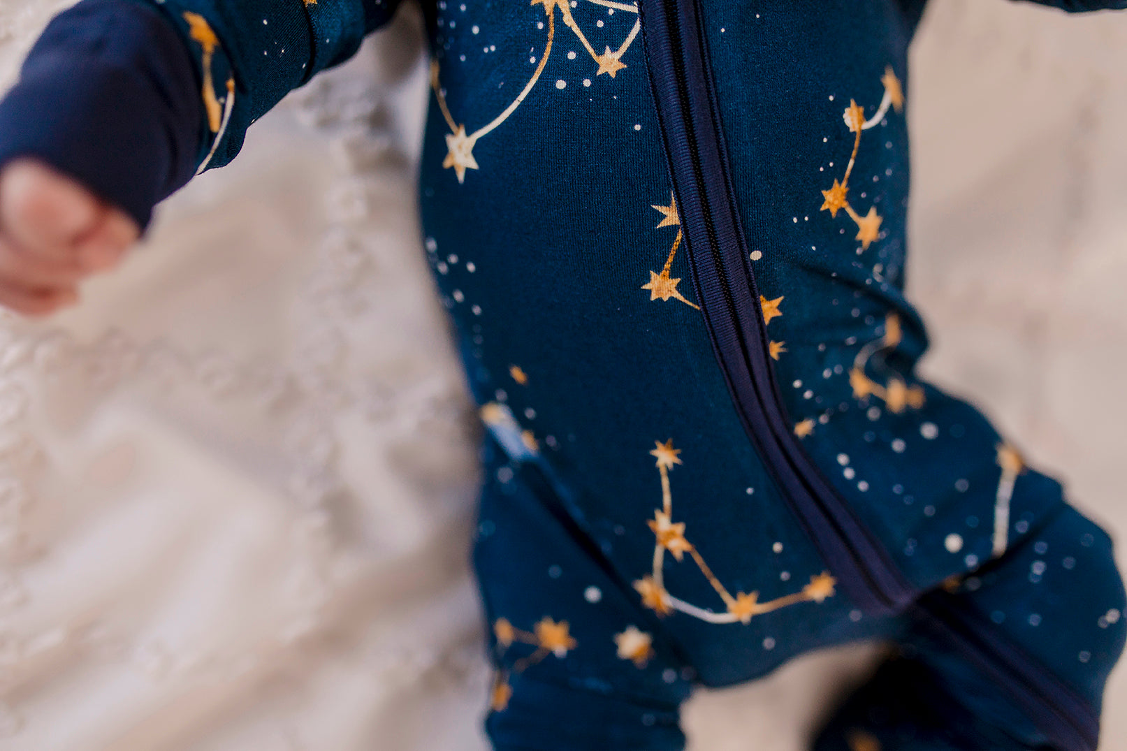 One piece pajamas set with yellow stars, yellow and white constellations, and the galaxy on a dark blue background with blue cuffs 