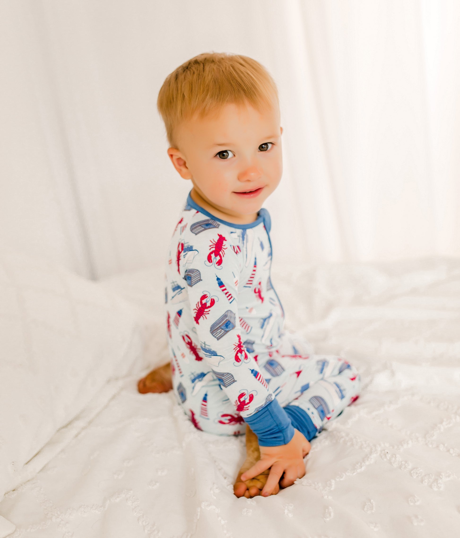 Child wearing a maine themed lobster fishing one piece with a light blue background and a darker blue on the cuffs 