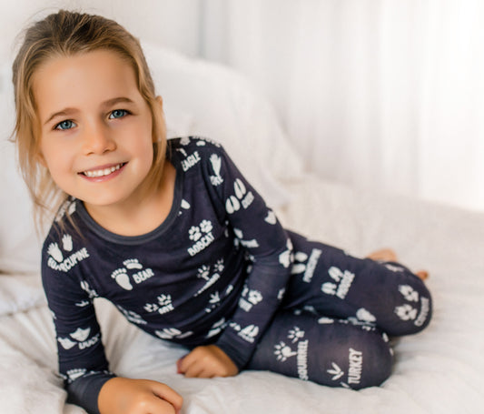 Child wearing dark grey pajamas with white animals tracks on a white blanket