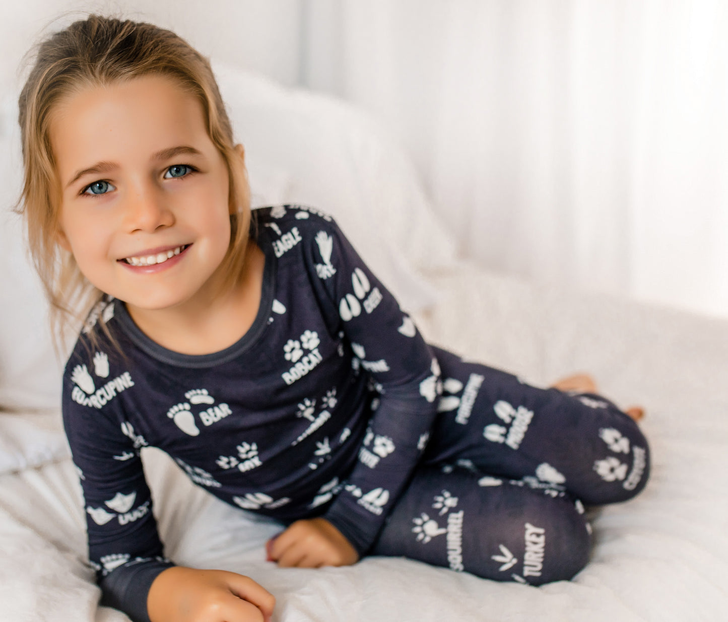Child wearing dark grey pajamas with white animals tracks on a white blanket