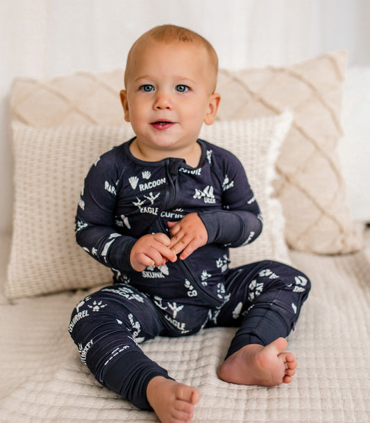 Baby wearing gray pajamas with white text and graphics, sitting on a beige couch