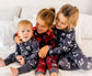 Three children in woodland themed bamboo pajamas sitting on a bed 