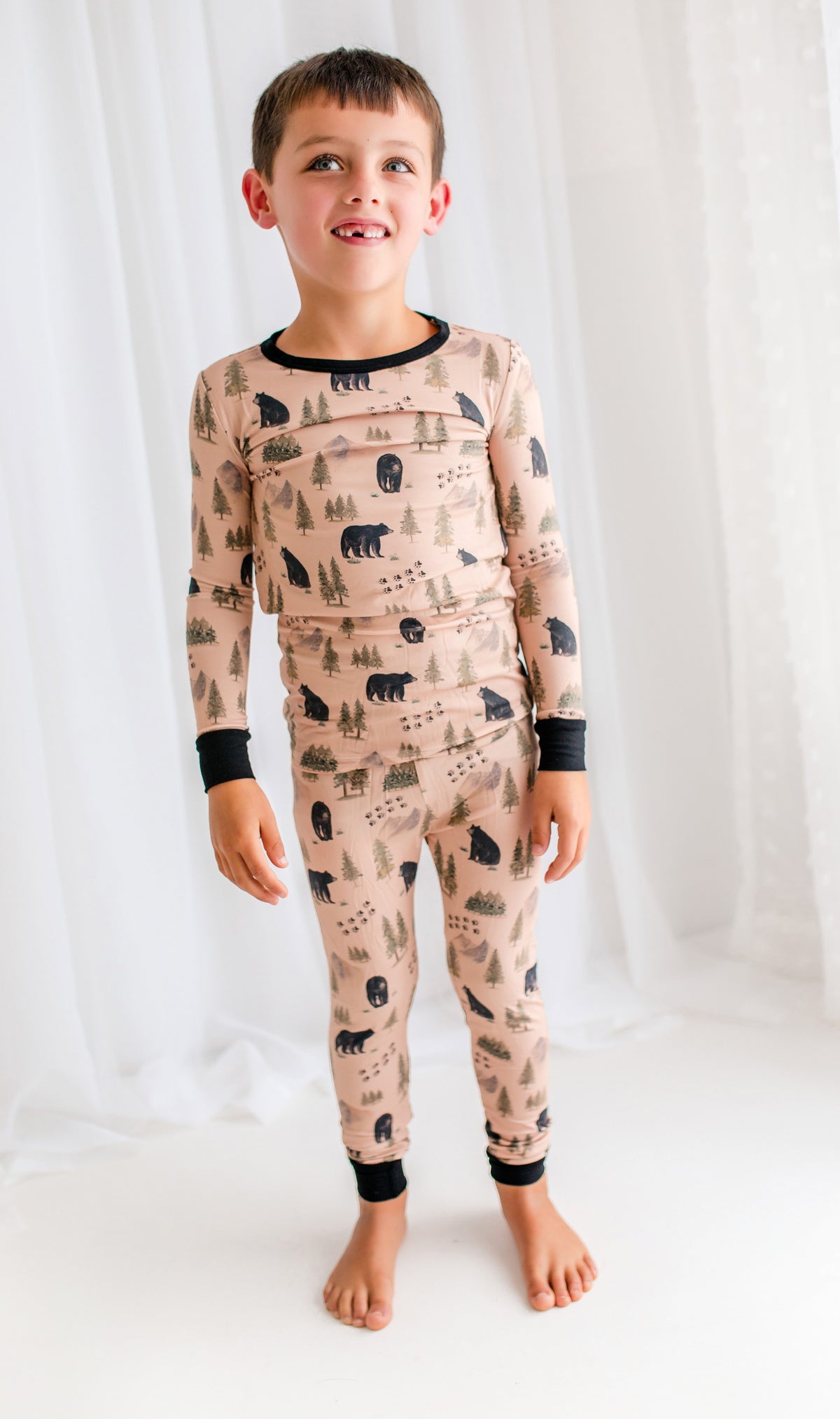 Child wearing a pajama set with Maine black bear, vast mountains, wilderness trees, and bear tracks on a tan background