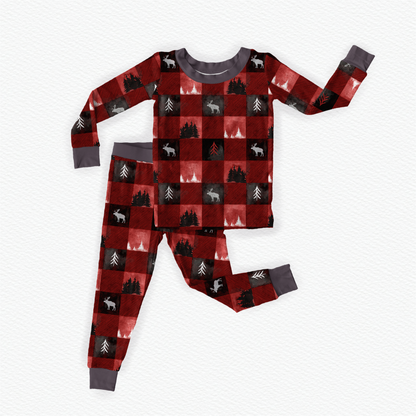 Children's long sleeve pajama set with red and black checkered pattern with white moose on the black squares and different kind of trees on the red and black squares with gray accents 