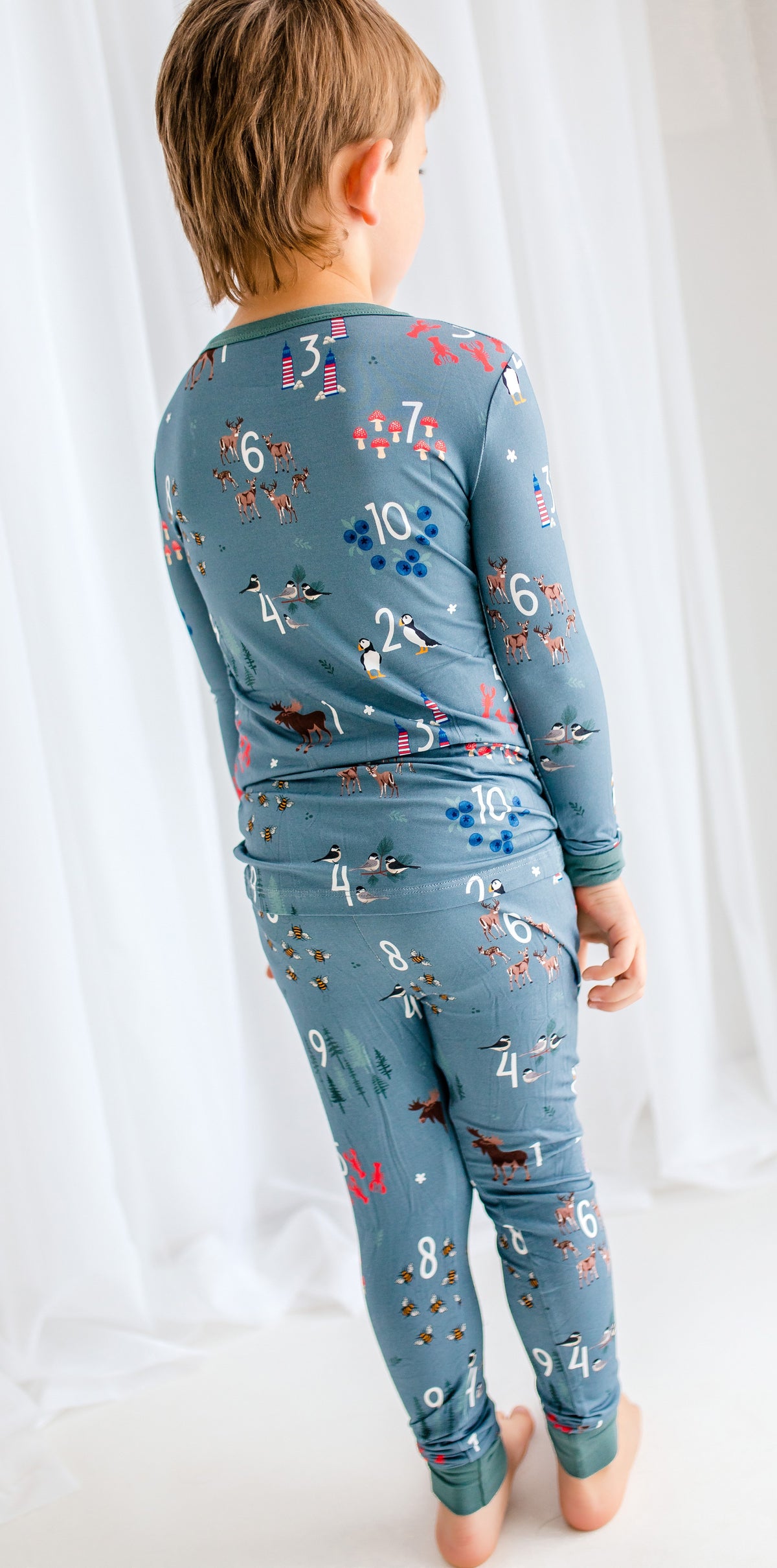 Child wearing a grey long-sleeve shirt and pants with numbers and animals and other Maine themes printed on them. 