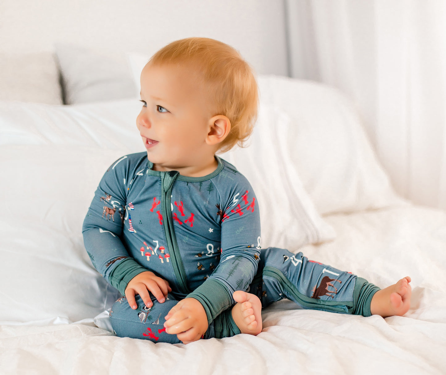 Baby wearing a light gray one piece with a bunch of items printed on it that represent all things Maine and counting numbers 1-10 